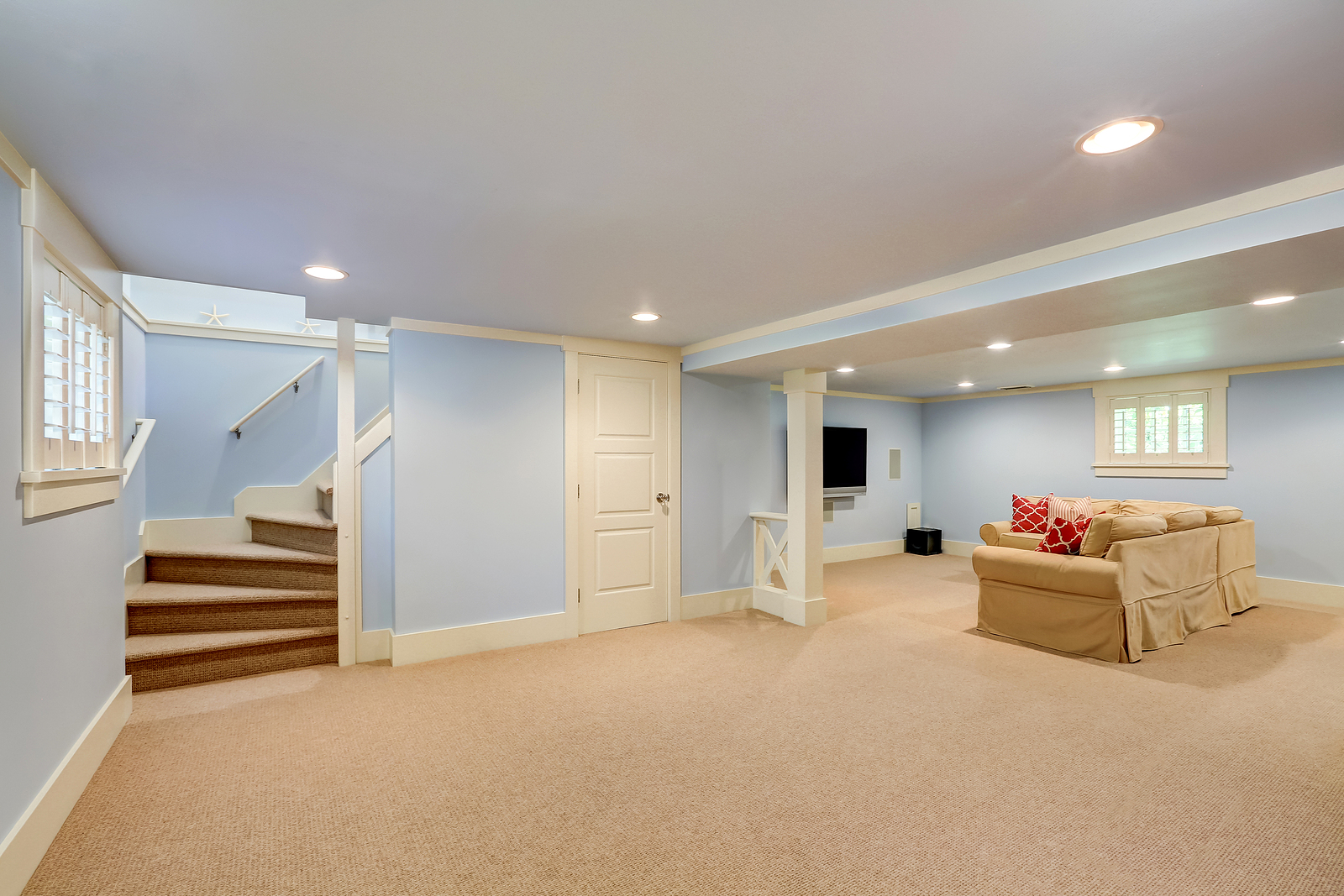 Spacious basement room interior in pastel blue tones. Beige carpet floor and large corner sofa with TV. Northwest USA