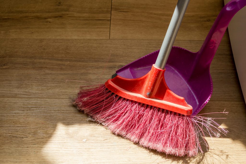Picture of a broom and a dust pan on vinyl plank flooring.