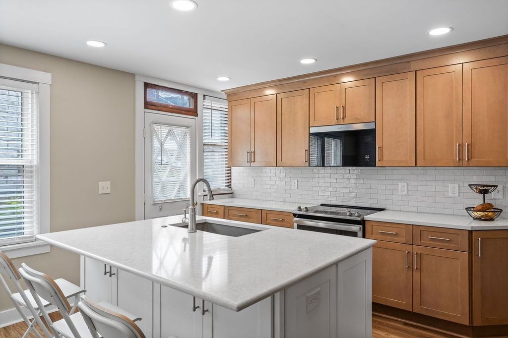 The Venetia Kitchen Features Light Wood Cabinets, White Countertops, and White Tile Backsplash for a Clean and Modern Design Focusing on Functionality and Comfort.