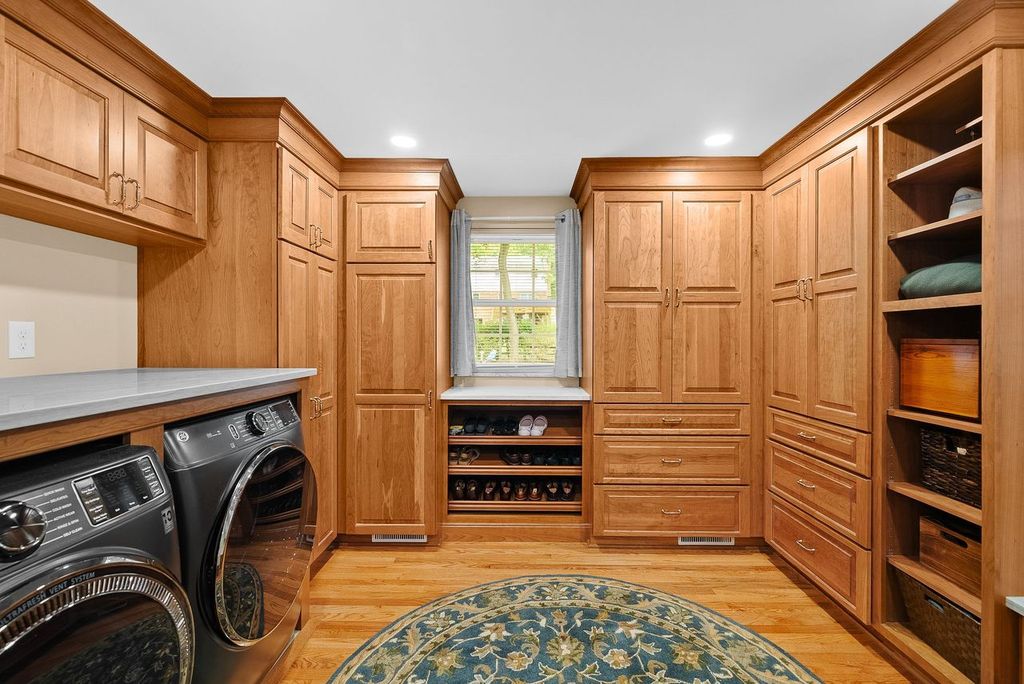 South Park Custom Laundry Room with Walk-In Closet Boasts Wood Cabinetry in a Warm Natural Finish, Open Shelving for Folding Items, Baskets and Decorated Touches Blending Practicality of a Laundry Room with the Elegance of a Stylish Dressing Space.