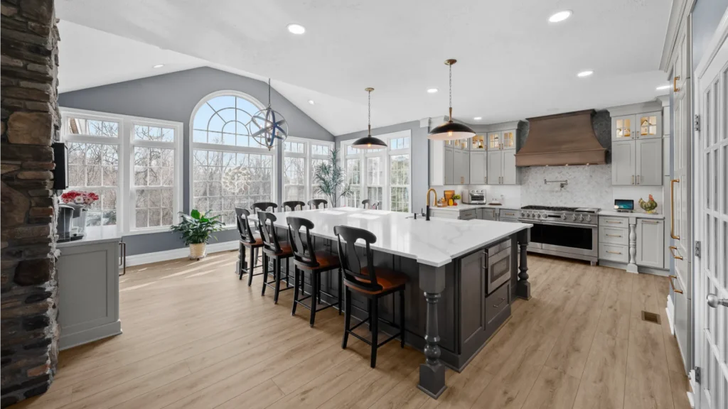Bright Airy Baldwin Kitchen Showing a Light Quartz Countertop With Veining, Warm Tone Luxury Vinyl Flooring and Large Gray Island