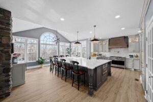 Bright Airy Baldwin Kitchen Showing a Light Quartz Countertop With Veining, Warm Tone Luxury Vinyl Flooring and Large Gray Island