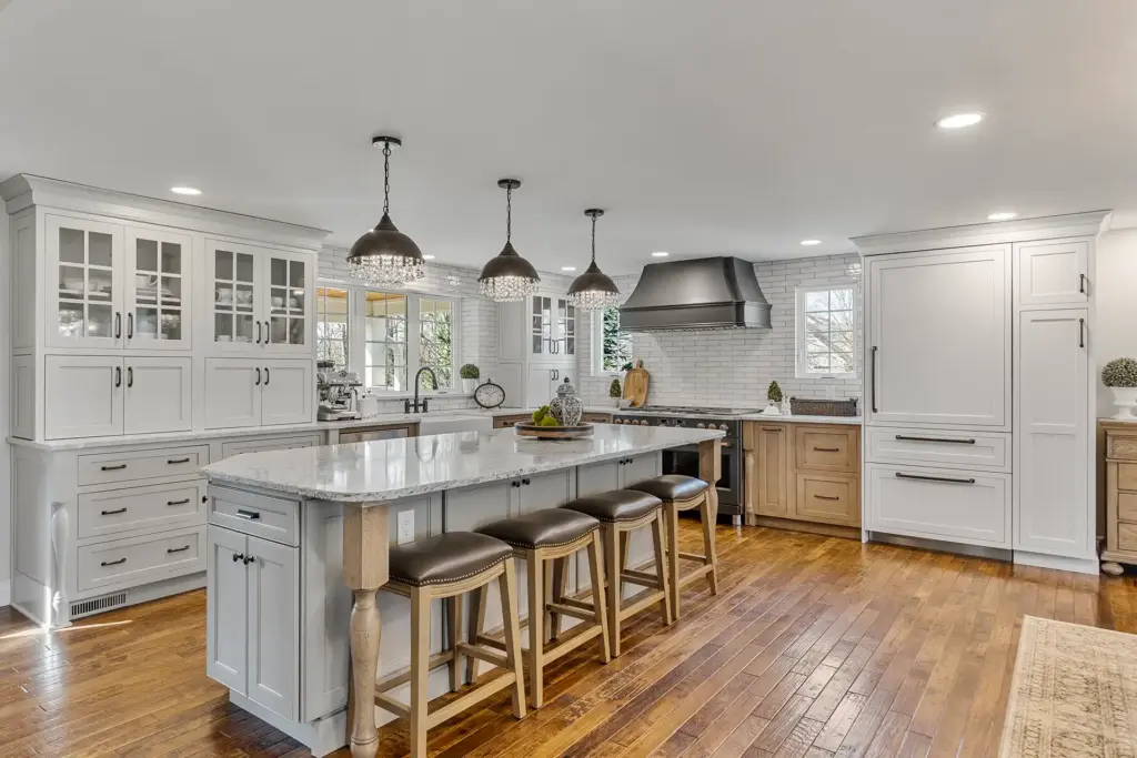 Bright Transitional Farmhouse Kitchen With Mix of White, Light Gray and Stain Shaker Cabinets, Quartz Countertop With Veining, Hardwood Floors and a Large Island.