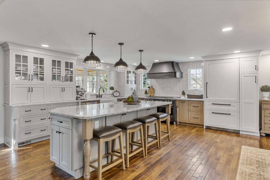 Bright Transitional Farmhouse Kitchen With Mix of White, Light Gray and Stain Shaker Cabinets, Quartz Countertop With Veining, Hardwood Floors and a Large Island.