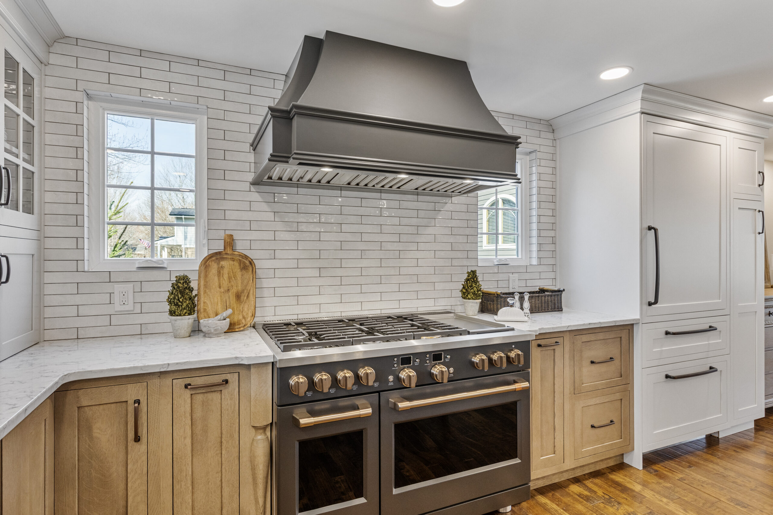 Bright Transitional Farmhouse Kitchen With Mix of White, Light Gray and Stain Shaker Cabinets, Quartz Countertop With Veining, Hardwood Floors and a Large Island.