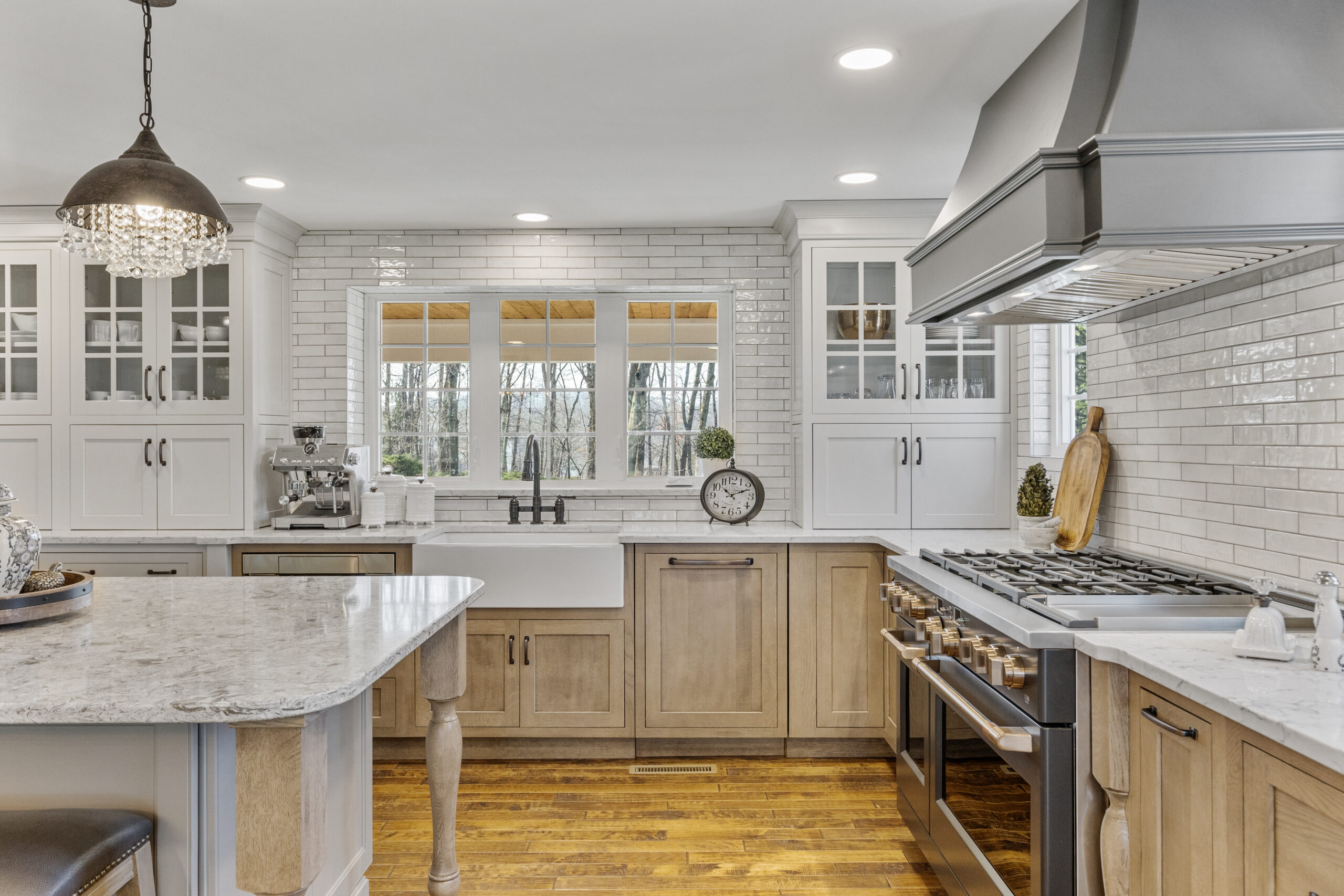 Bright Transitional Farmhouse Kitchen With Mix of White, Light Gray and Stain Shaker Cabinets, Quartz Countertop With Veining, Hardwood Floors and a Large Island.