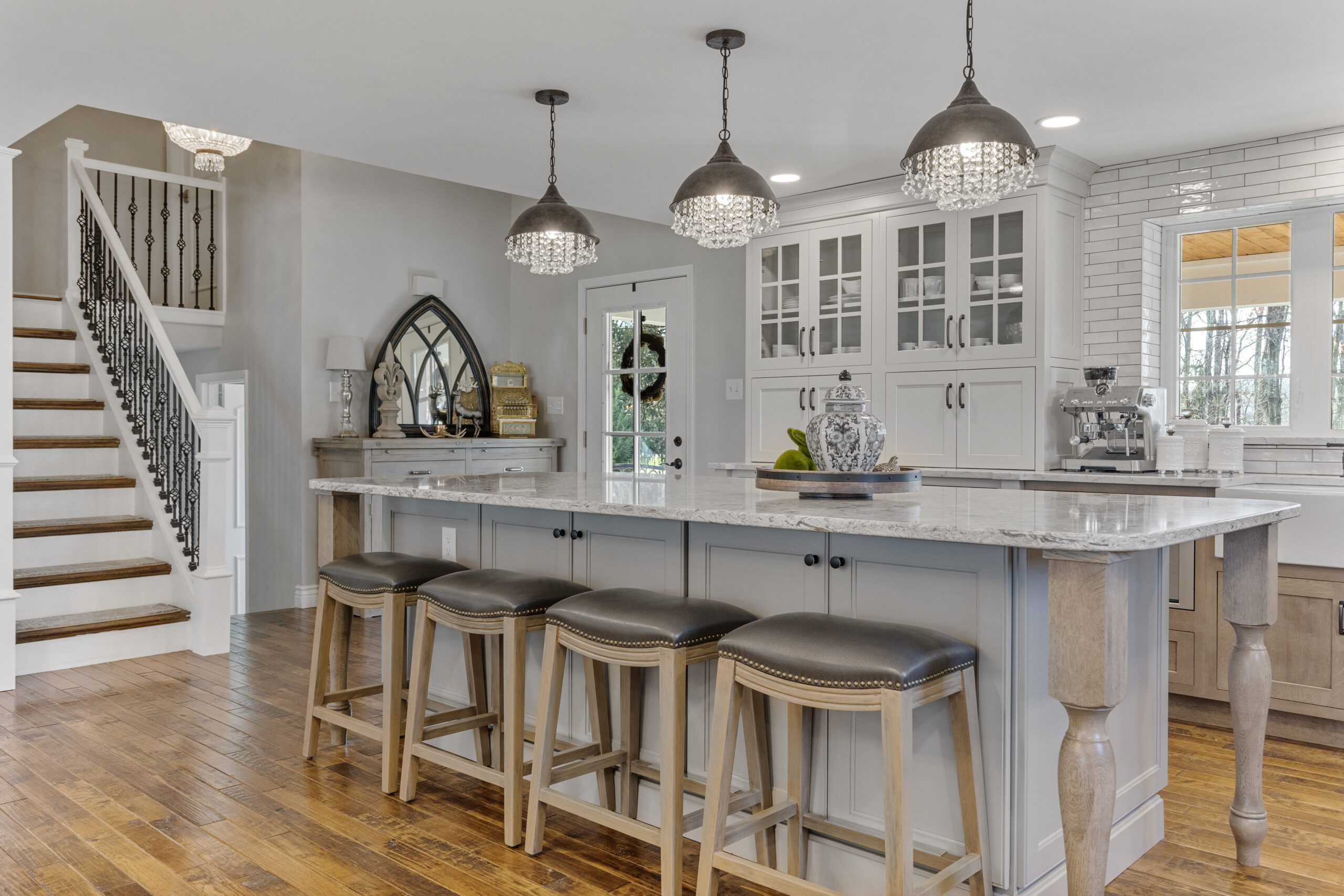 Bright Transitional Farmhouse Kitchen With Mix of White, Light Gray and Stain Shaker Cabinets, Quartz Countertop With Veining, Hardwood Floors and a Large Island.