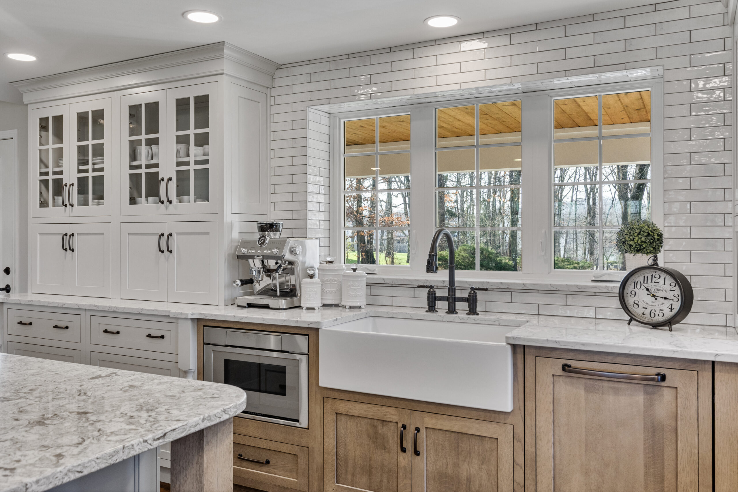Bright Transitional Farmhouse Kitchen With Mix of White, Light Gray and Stain Shaker Cabinets, Quartz Countertop With Veining, Hardwood Floors and a Large Island.