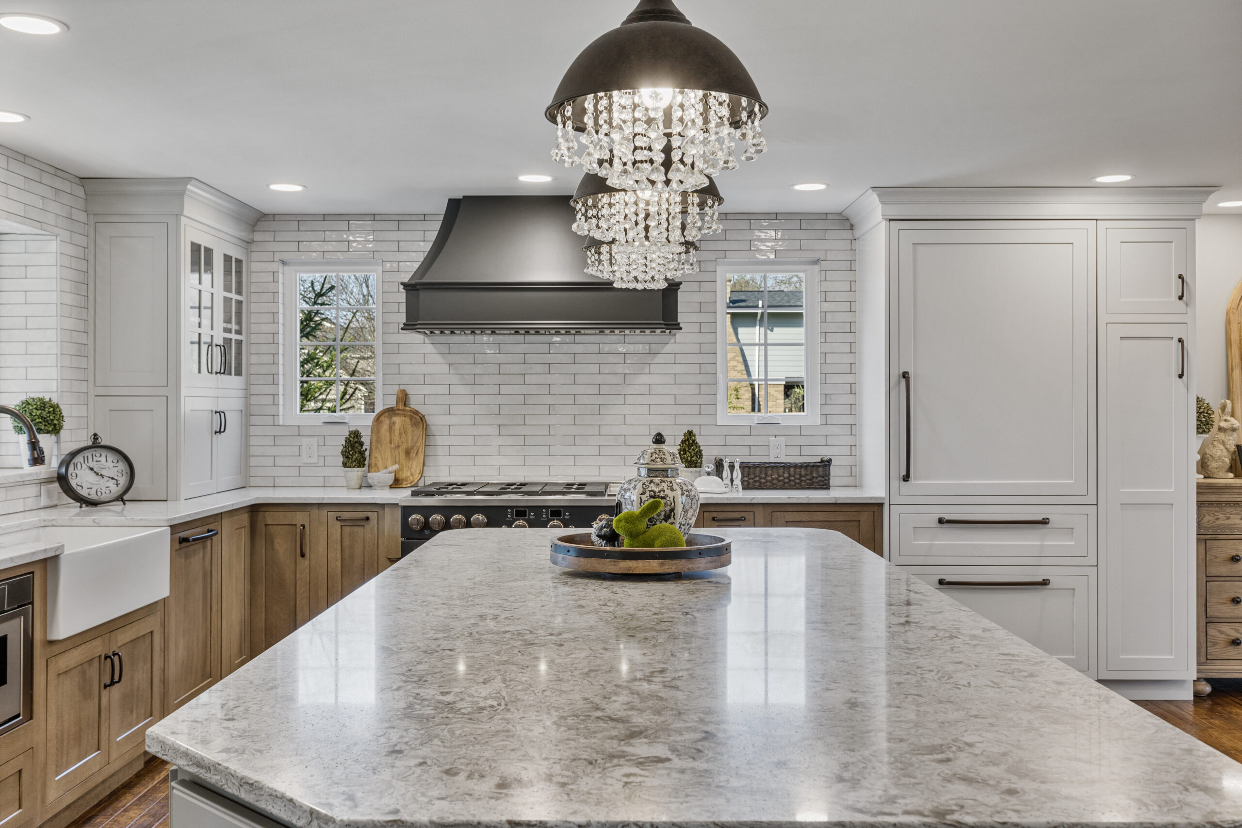 Bright Transitional Farmhouse Kitchen With Mix of White, Light Gray and Stain Shaker Cabinets, Quartz Countertop With Veining, Hardwood Floors and a Large Island.