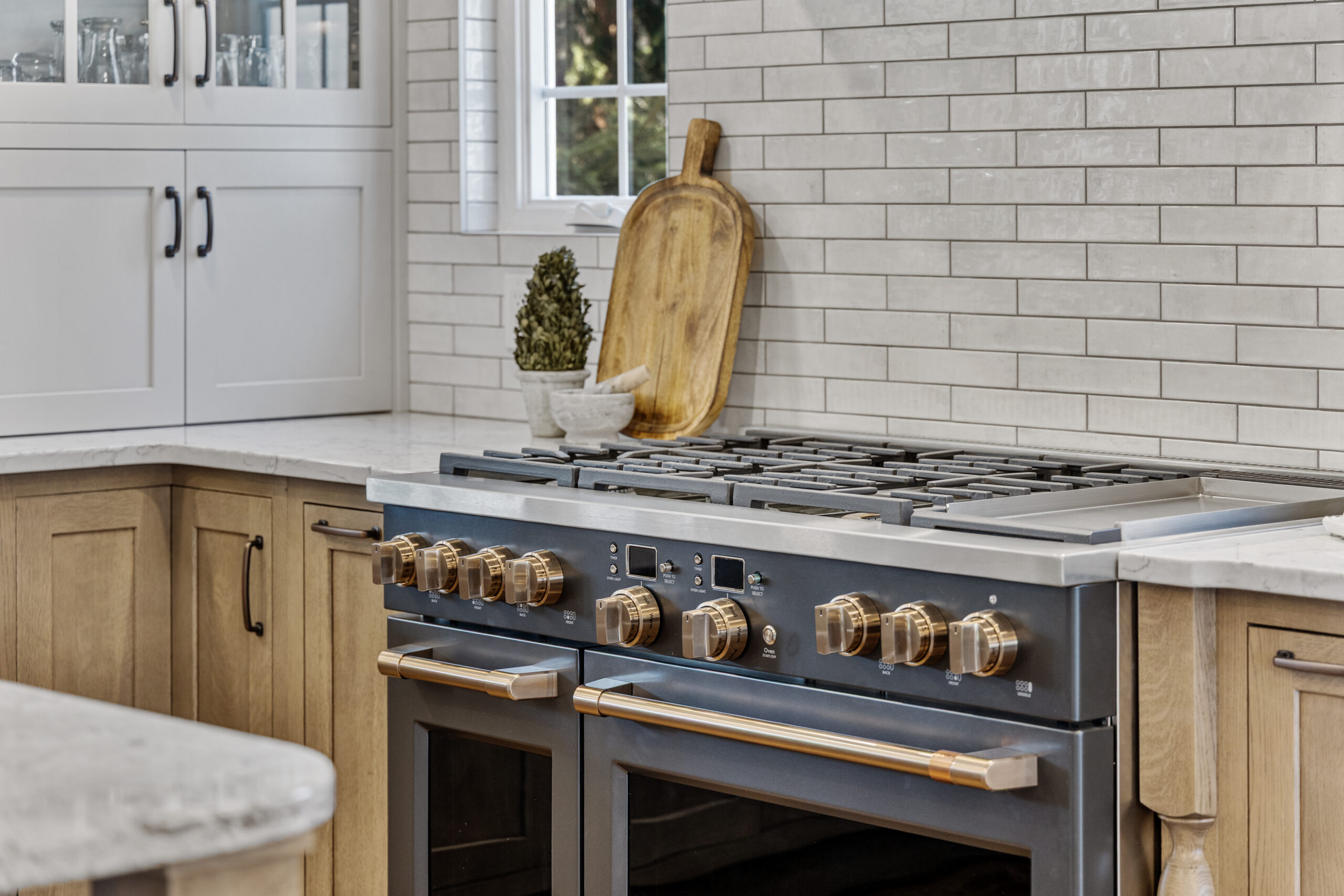 Bright Transitional Farmhouse Kitchen With Mix of White, Light Gray and Stain Shaker Cabinets, Quartz Countertop With Veining, Hardwood Floors and a Large Island.