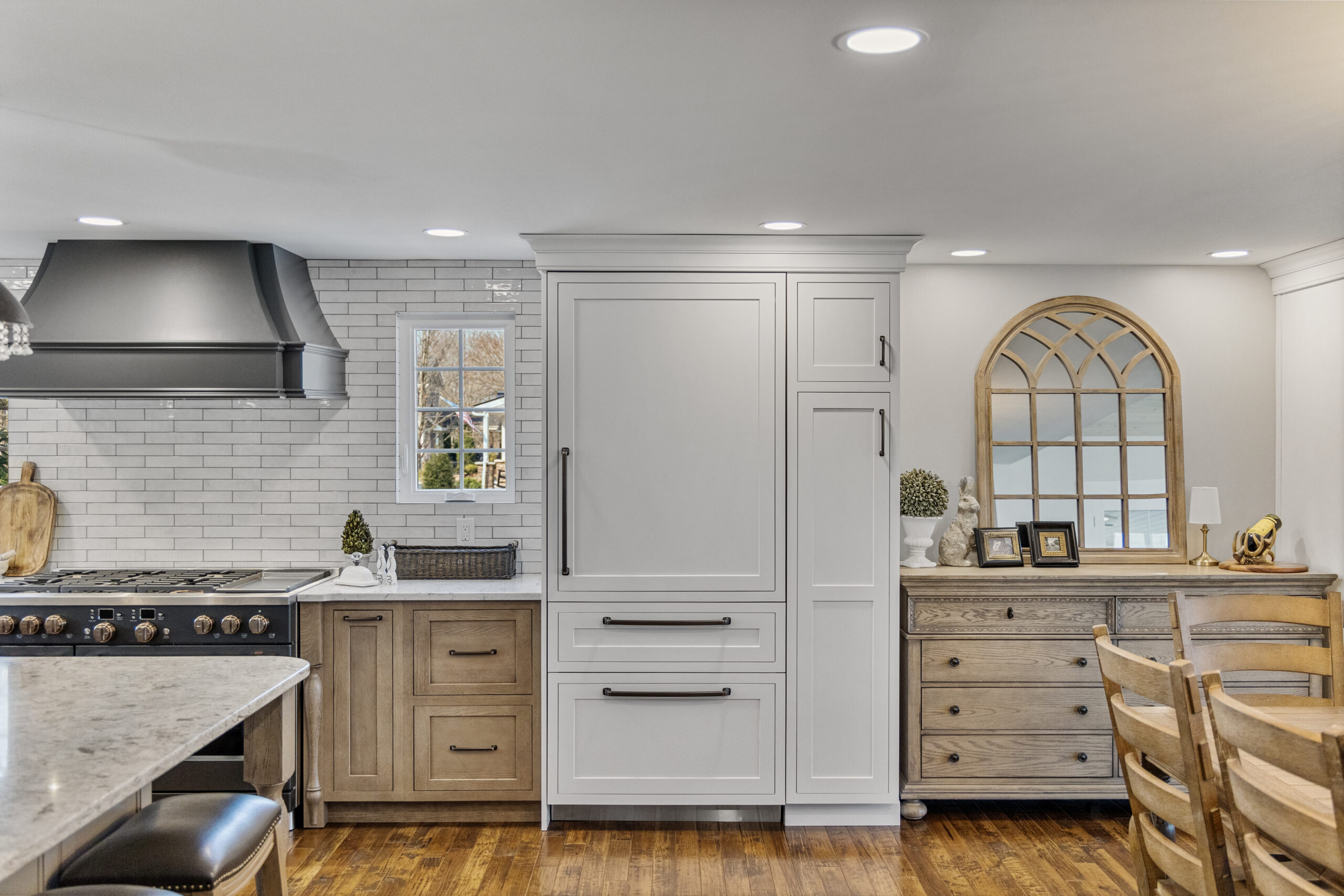 Bright Transitional Farmhouse Kitchen With Mix of White, Light Gray and Stain Shaker Cabinets, Quartz Countertop With Veining, Hardwood Floors and a Large Island.