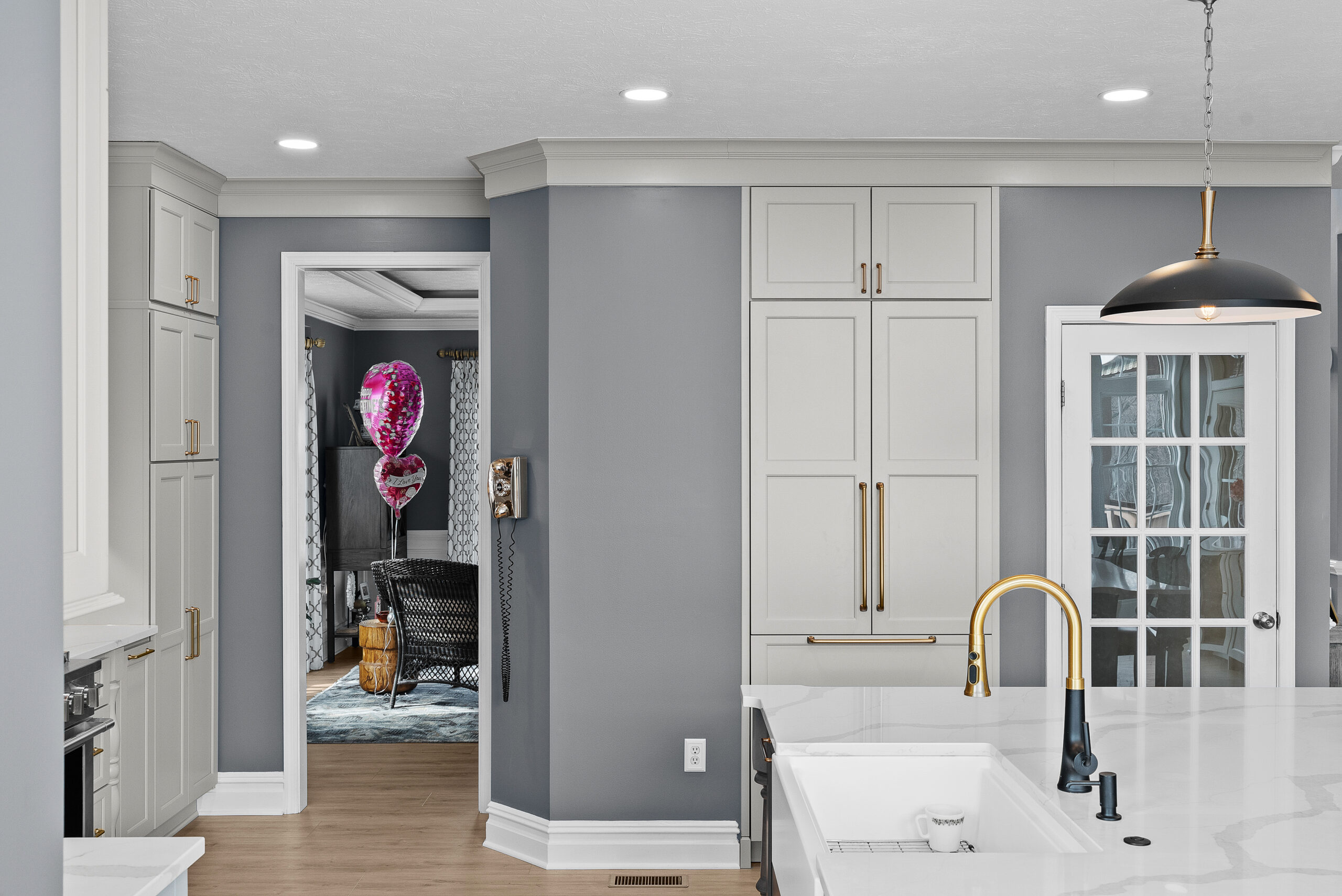 Bright Airy Baldwin Kitchen Showing a Light Quartz Countertop With Veining, Warm Tone Luxury Vinyl Flooring and Large Gray Island